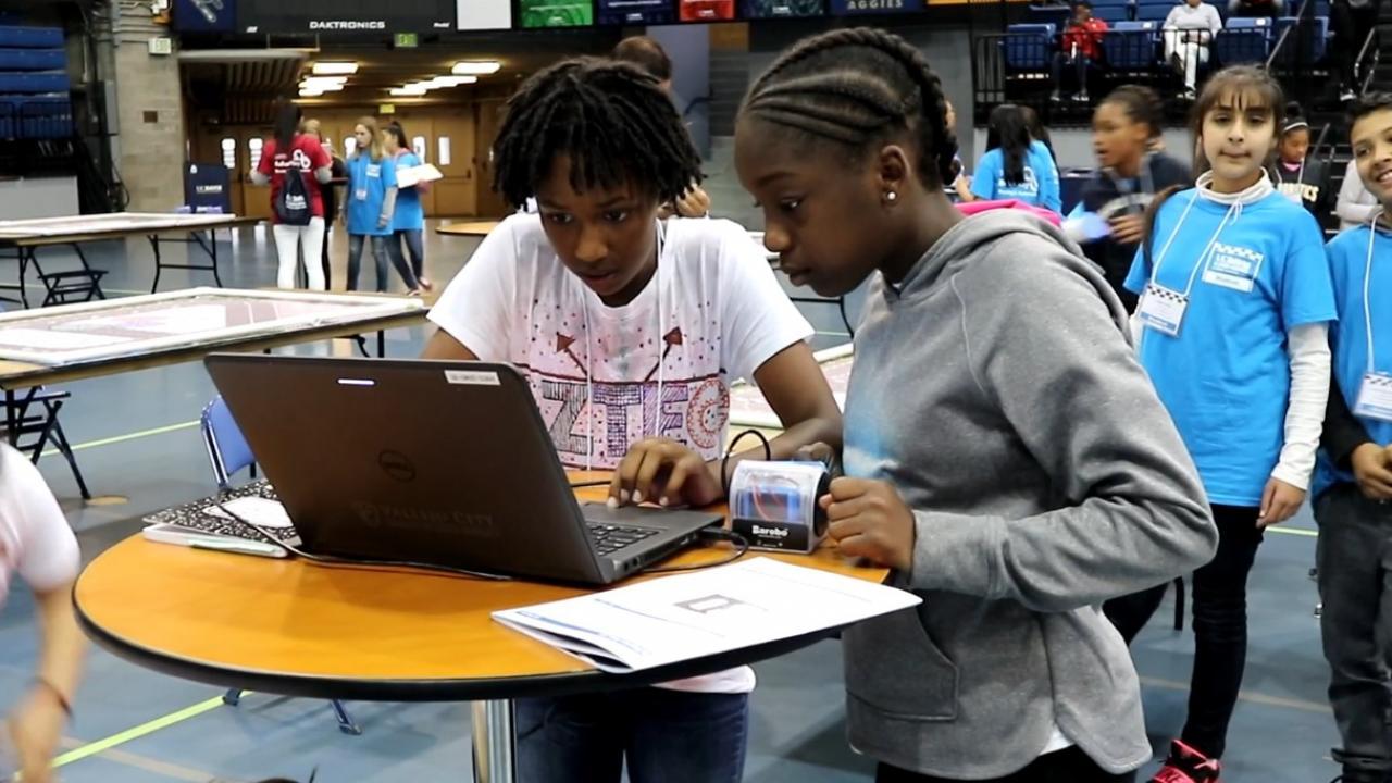 a group of young african-american girls looking at a computer set up at a table