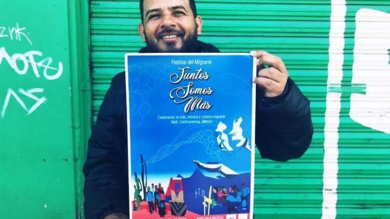 a man holding a poster that says Juntos Somos Mas in front of a green garage door
