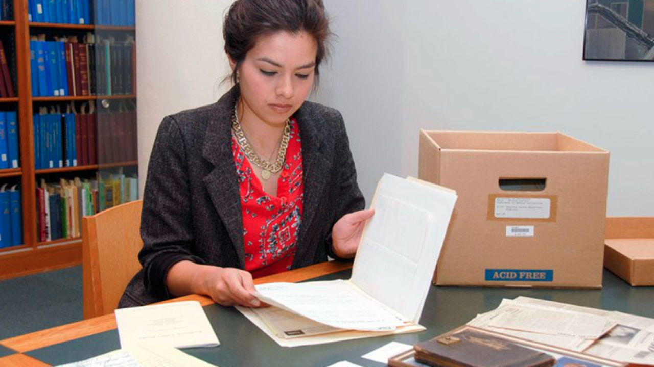 Women in a red shirt and gray jacket looking at a file folder and papers.