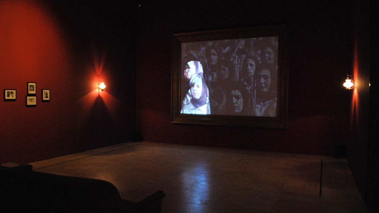 A room with two lights on the side of the walls with a projection of a group of women in the middle