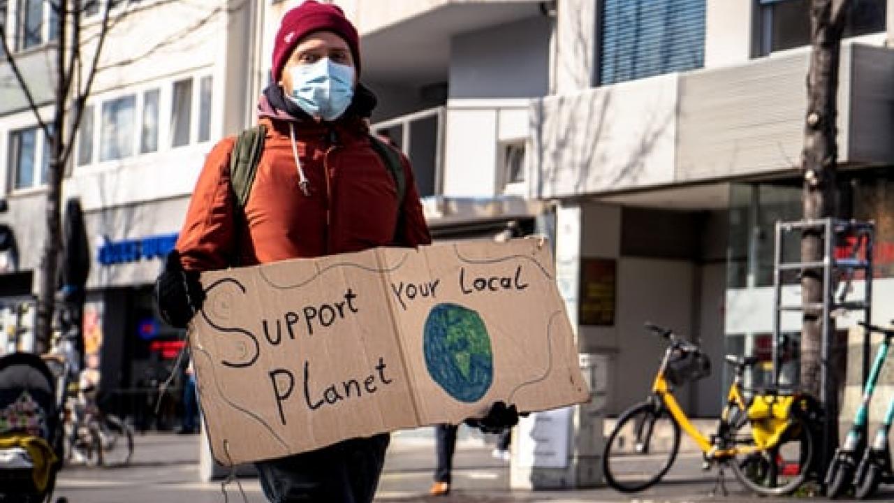 a man in a mask holding a sign that says support your local planet