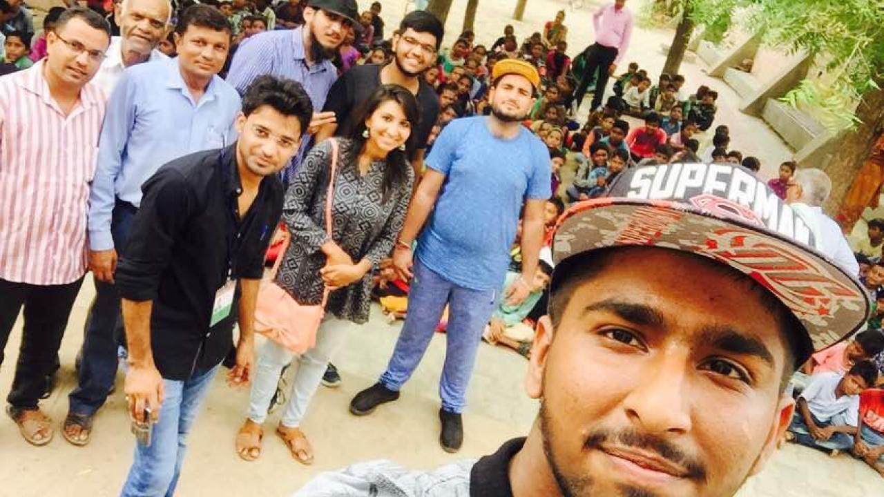 a man in a hat taking a selfie with a group of Indian villagers behind him
