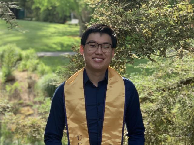 Jonathan smiling on a bench while wearing a gold UC Davis stole 