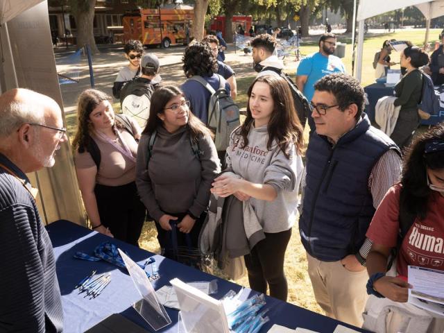 Luis Carvajal-Carmona and three students at a booth at the Graduate and Law School Fair on the Quad. Three female students talk with two male professors at tabling event on UC Davis quad. Another female student is reading a brochure.
