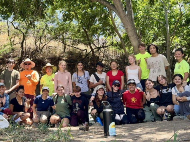A group of students and adults pose together under a tree.