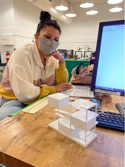 Woman sits at a table behind a model of a house