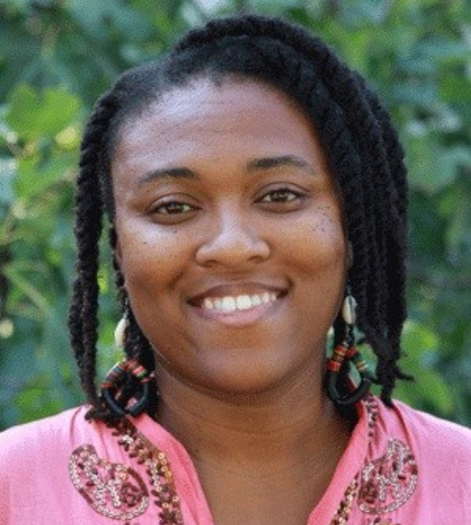 Close up headshot of a woman smiling outside. She is wearing a blouse with detailed beads on it.