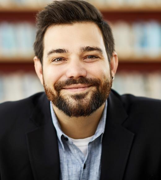 close up of a man smiling in front of a blurred background of books