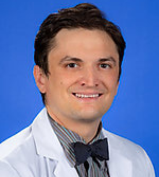 Close up headshot of a man smiling. He is wearing a white coat with a bowtie.