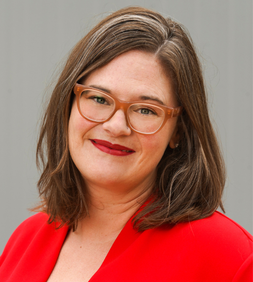 Close up headshot of a woman wearing glasses smiling in front of a plain background