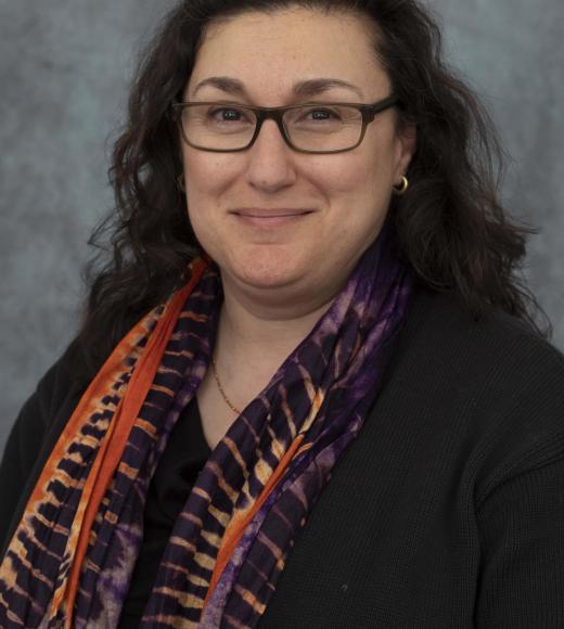 Woman wearing glasses and a scarf smiles directly into the camera close up