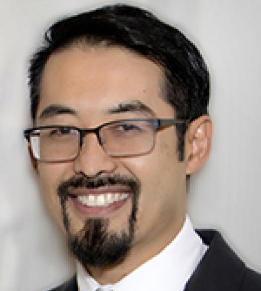 Man in glasses smiles directly into the camera wearing a suit in front of a plain background
