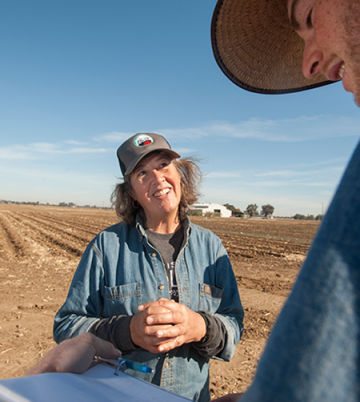 a woman in a denim shirt standing in a field talking to a young man in a hat