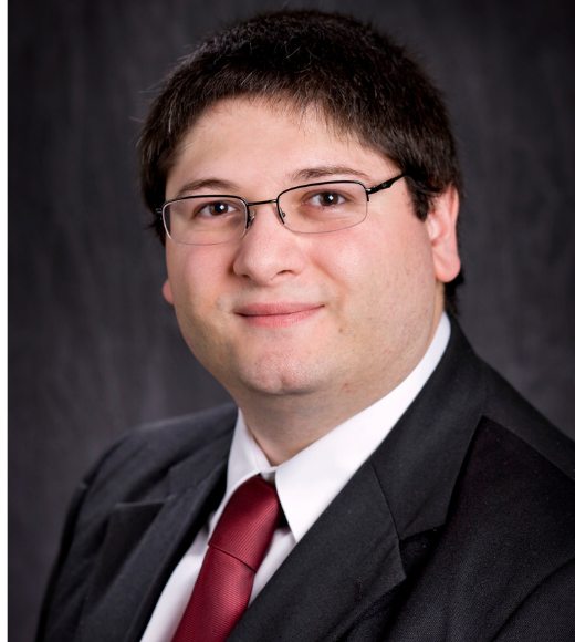 Close up headshot of a man wearing glasses and a suit in front of a plain background