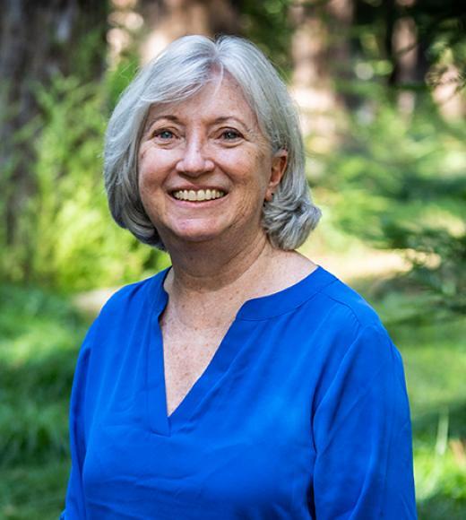 Woman in a long sleeve shirt smiles directly into the camera in front of a blurry nature background