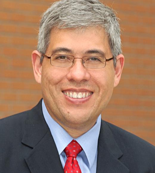 Gabriel “Jack” Chin wearing a suit and red tie smiling in front of a brown background