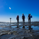 three people walking across wet ground with a blue sky 
