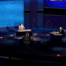 a debate stage with three people sitting far apart wearing masks