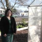 woman smiling while standing in front of a greenhouse at a school