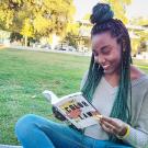 a young african american woman sitting on grass reading a book