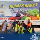 A group of individuals pose in front of a large truck featuring fruits and the words "Hunger Heroes Feed Hope!"