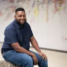 Aron King smiling while sitting on a bench in front of a mural
