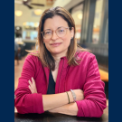 Desirée Martín, associate professor of English at UC Davis, is sitting in a cafe. Her arms are crossed and she is wearing glasses and a pink shirt.