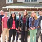 Group of nine individuals smile side by side for a group photo outside of a building