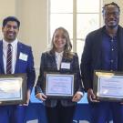Three graduate students standing side by side holding their awards