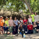 A group of students and adults pose together under a tree.