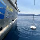 White secchi disc hanging from cord off research vessel labeled UC Davis Tahoe Environmental Research Center hovers over surface of blue Lake Tahoe