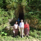 Three individuals stand outside in front of a cave full of leaves and grass