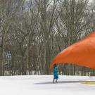 a snowy field with people spread out holding a large orange cloth