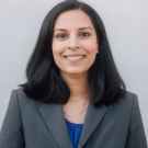 Close up headshot of a woman wearing a blazer in front of a plain background