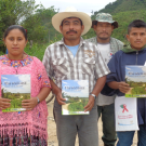 Woman in bright pink blouse stands with three men for a group photo. Individuals hold a pamphlet featuring a nature trail.
