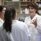 Woman in white lab coat talks to two other women in white lab coats
