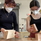 Students holding blocks to build a block scale model while wearing masks and safety glasses