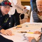 A group of adults gathered around a table play a board game that looks like a map of the Tomales community