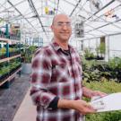 Man holding clipboard inside of a greenhouse smiles