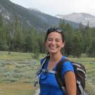 Woman wearing a backpack smiling in front of trees