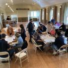 Five groups of individuals gather around five separate table playing a board game indoors at the Tomales Branch Library