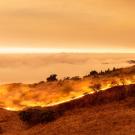 Orange smokey sky with marine layer and line of wildfire in California coastal hills