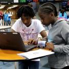 a group of young african-american girls looking at a computer set up at a table 