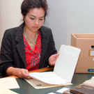 Women in a red shirt and gray jacket looking at a file folder and papers.