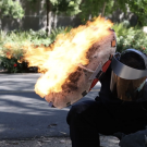 a person in a superhero costume using a shield to protect themselves against fire