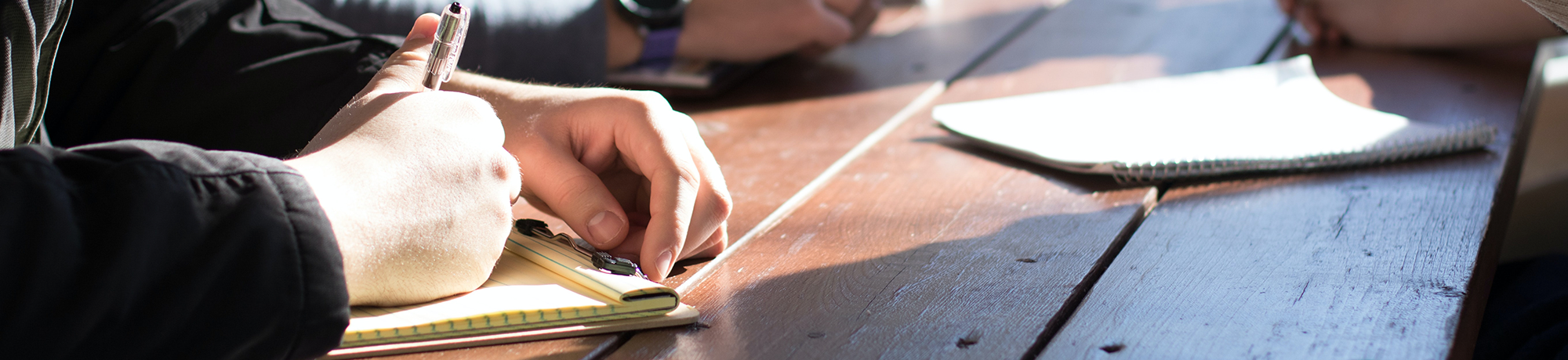 a wood table with peoples hands writing in notebooks. Photo by Dylan Gillis.